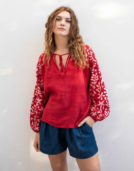 Female wearing a red blouse with embroidered sleeves in front of white wall