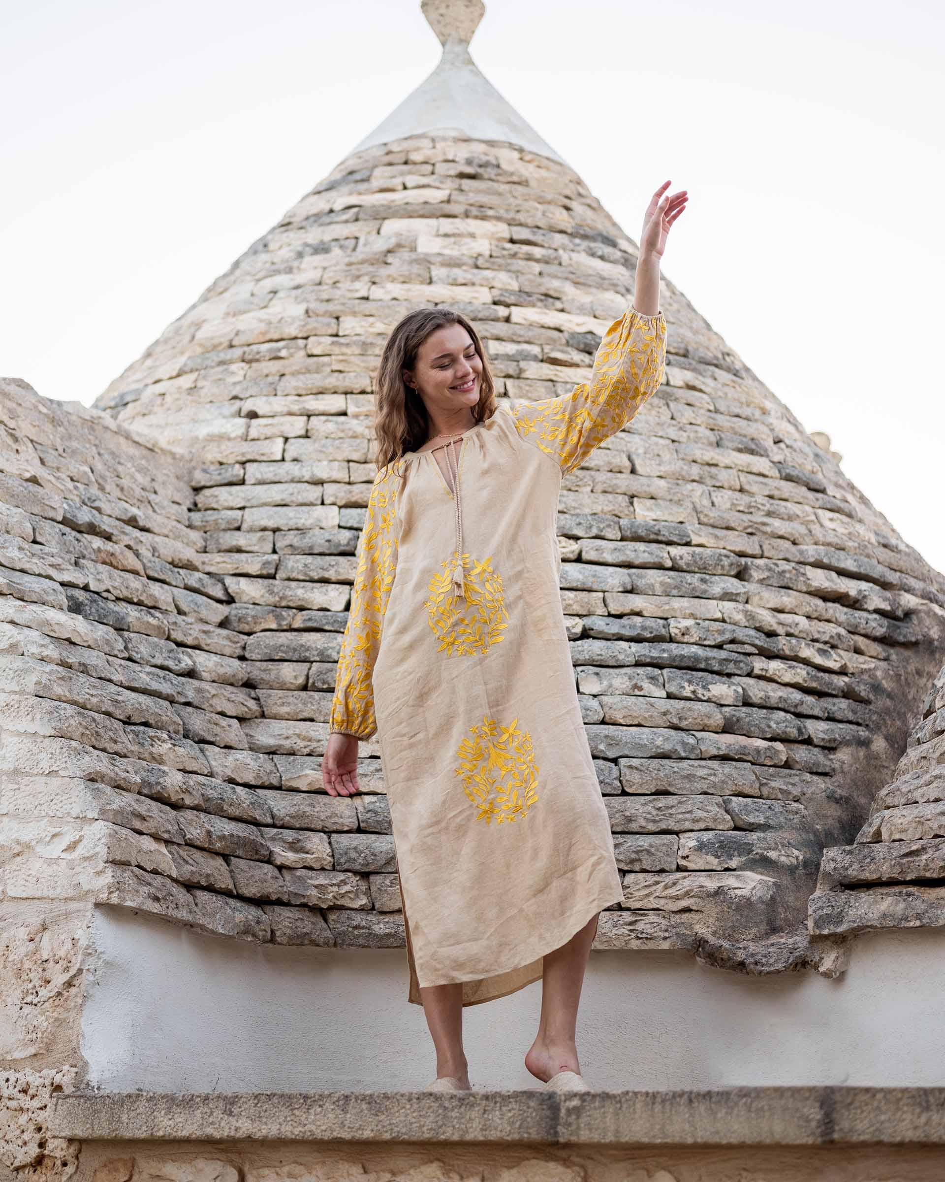 woman standing on ledge in tan and yellow maxi dress with embroidery