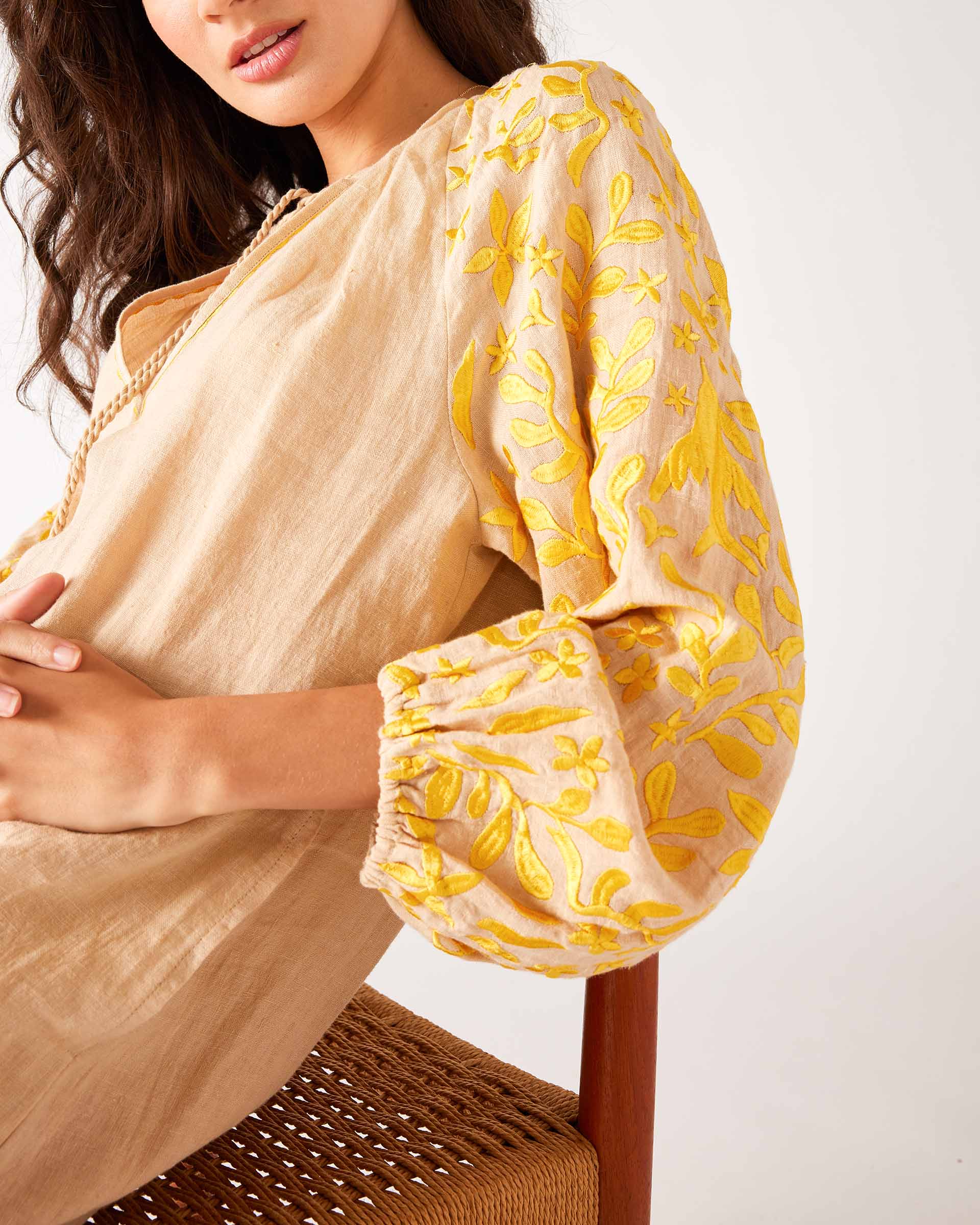 close up detail of woman wearing tan and yellow dress with embroidery