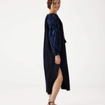 female standing sideways wearing Mersea black embroidered maxi dress with V-neck and tassel ties on a white background