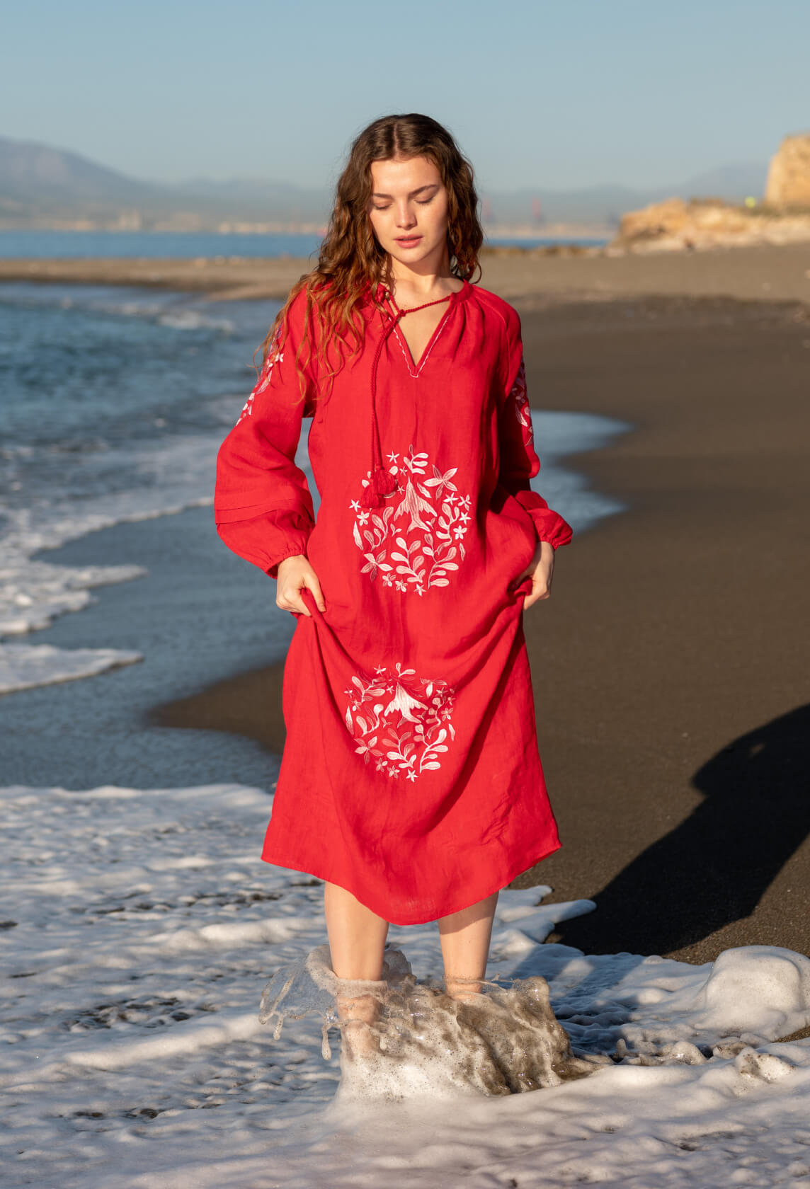female wearing a red maxi dress with embroidery standing in the water on the beach