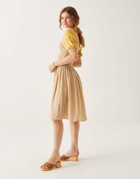  female wearing tan yellow smocked dress with white embroidery standing on a white background