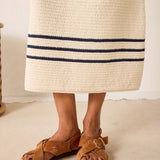 Brown sandals worn with a long beige skirt featuring blue stripes on a neutral background