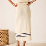 Person wearing a cream-colored knit skirt with blue stripes, standing against a plain background.