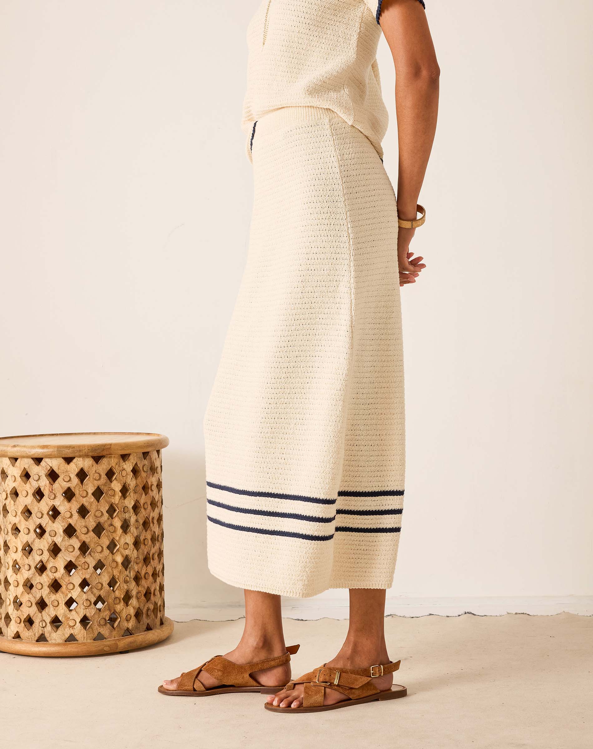 Person wearing a long, light-colored dress with a striped pattern, standing next to a woven stool.