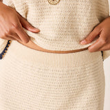 Close-up of a person adjusting a beige belt on a textured beige garment.