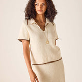 Woman wearing a beige outfit with a matching skirt on a plain background