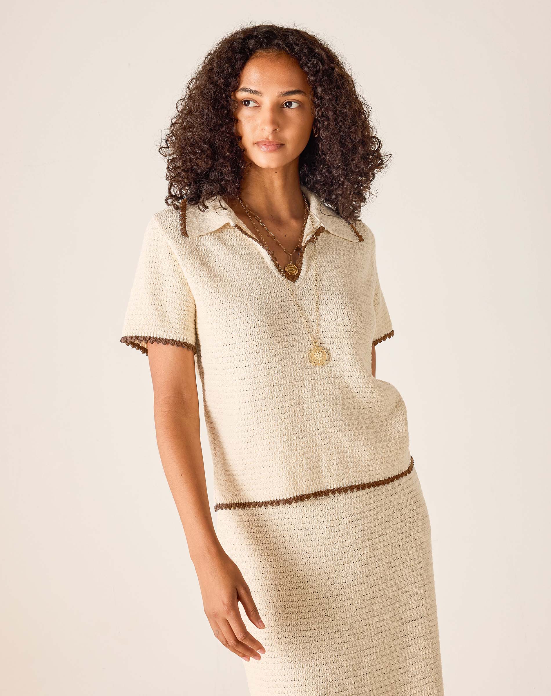 Woman wearing a beige outfit with a matching skirt on a plain background