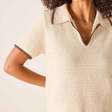 Woman wearing a beige knitted dress with brown trim on a light background