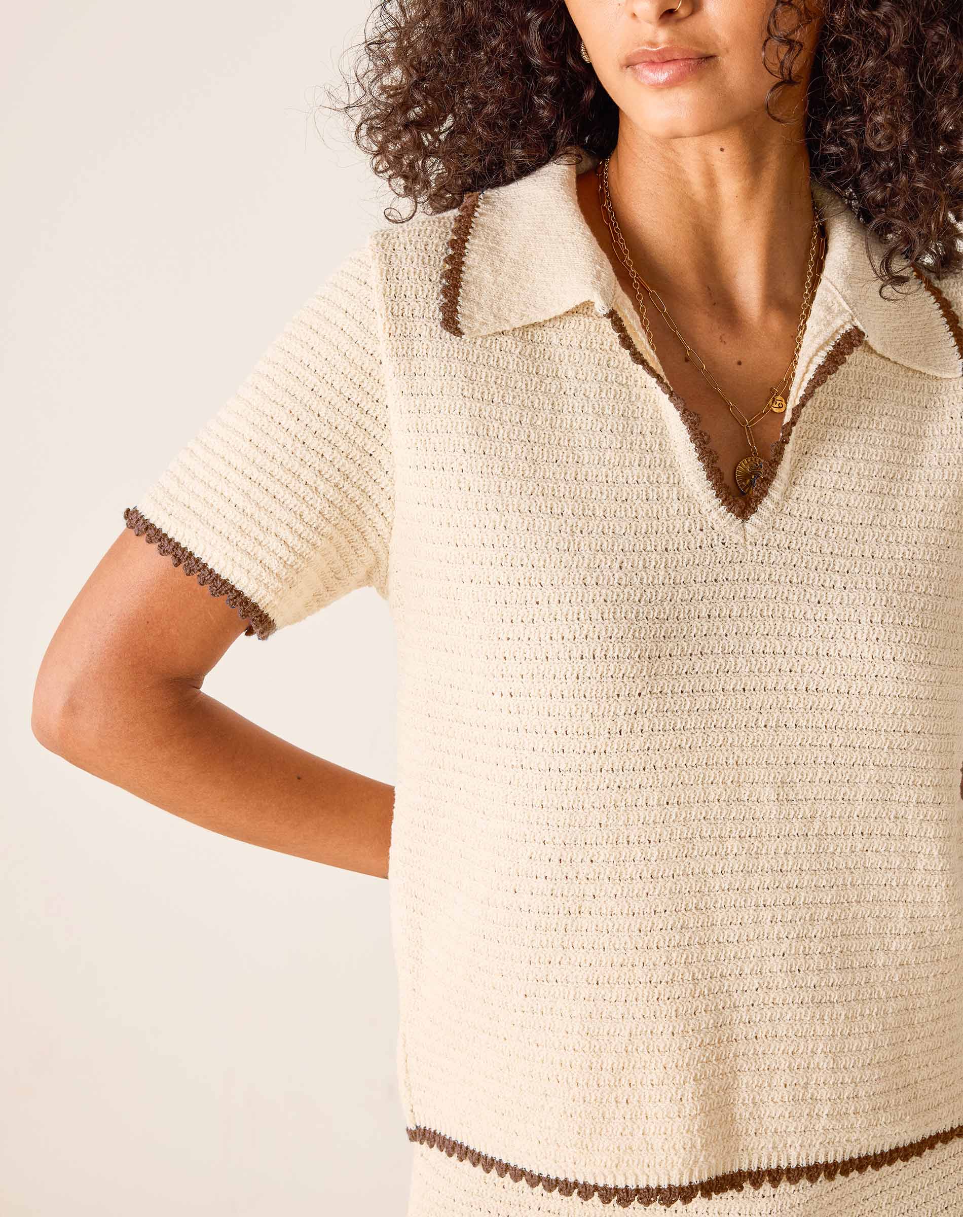 Woman wearing a beige knitted dress with brown trim on a light background
