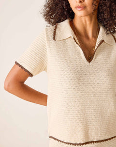 Woman wearing a beige knitted dress with brown trim on a light background