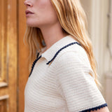 Woman wearing a white textured dress with navy trim outdoors.