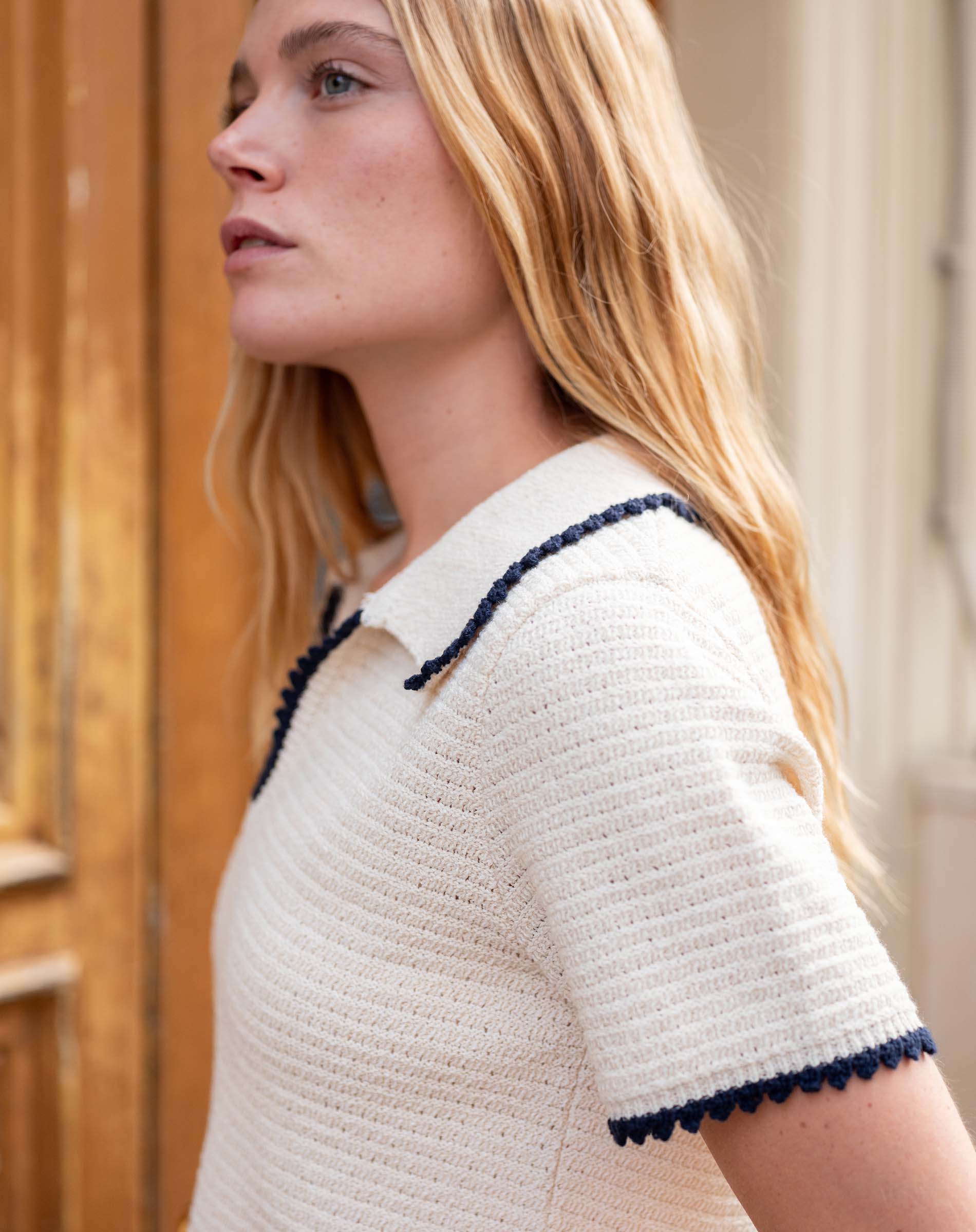 Woman wearing a white textured dress with navy trim outdoors.