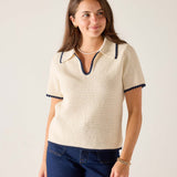 Woman wearing a cream-colored knit sweater with navy trim on a plain background