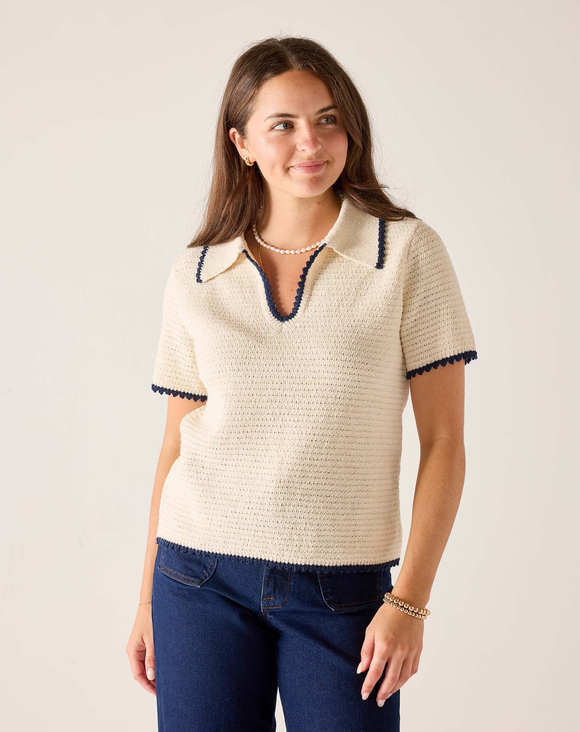 Woman wearing a cream-colored knit sweater with navy trim on a plain background