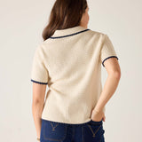 Woman wearing a cream-colored knit cardigan with navy trim on a plain background