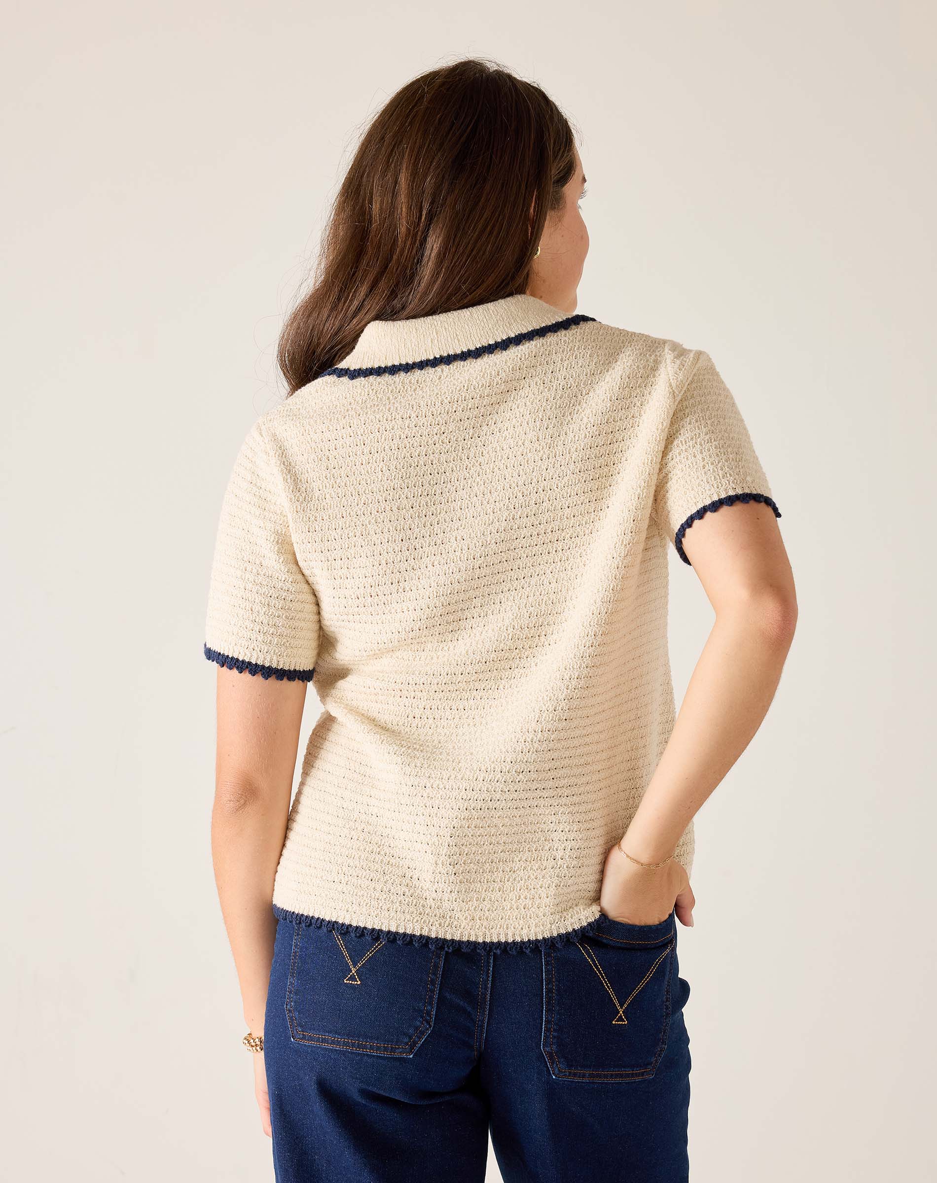 Woman wearing a cream-colored knit cardigan with navy trim on a plain background