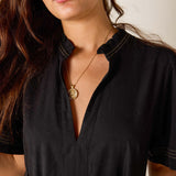 Woman wearing a black shirt with a gold necklace featuring a pendant.