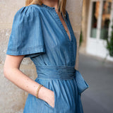 Woman wearing a blue dress with a stone wall and building in the background