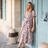 Woman in a floral dress standing in front of a blue door on a street.