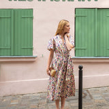 Woman in a floral dress standing on a street with a restaurant sign above.