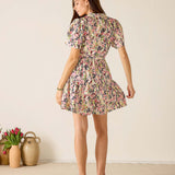 Woman wearing a floral dress standing in a minimalistic room with a vase of tulips.