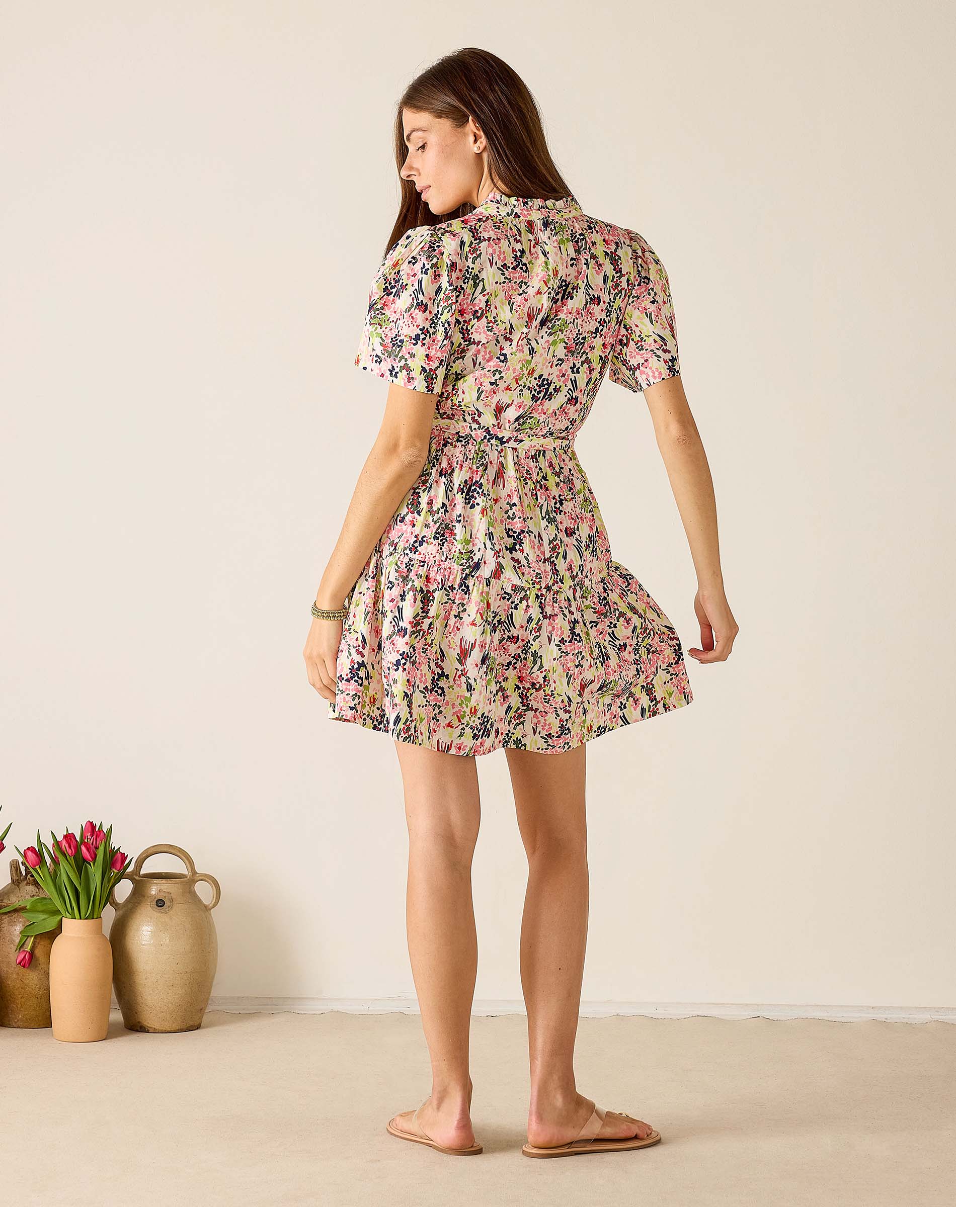 Woman wearing a floral dress standing in a minimalistic room with a vase of tulips.