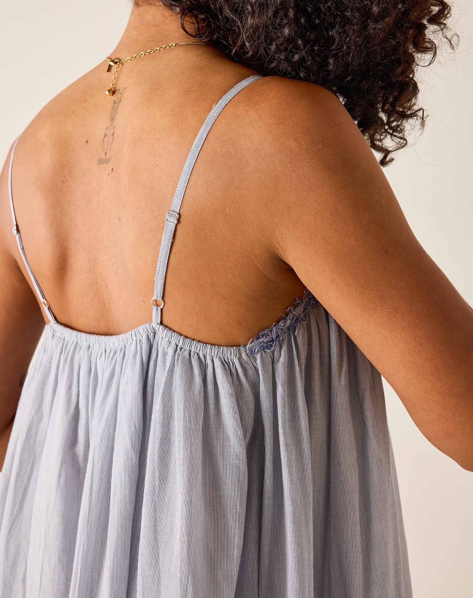 Woman wearing a light gray dress with thin straps on a neutral background
