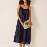 Woman wearing a navy blue dress holding a clutch against a white background