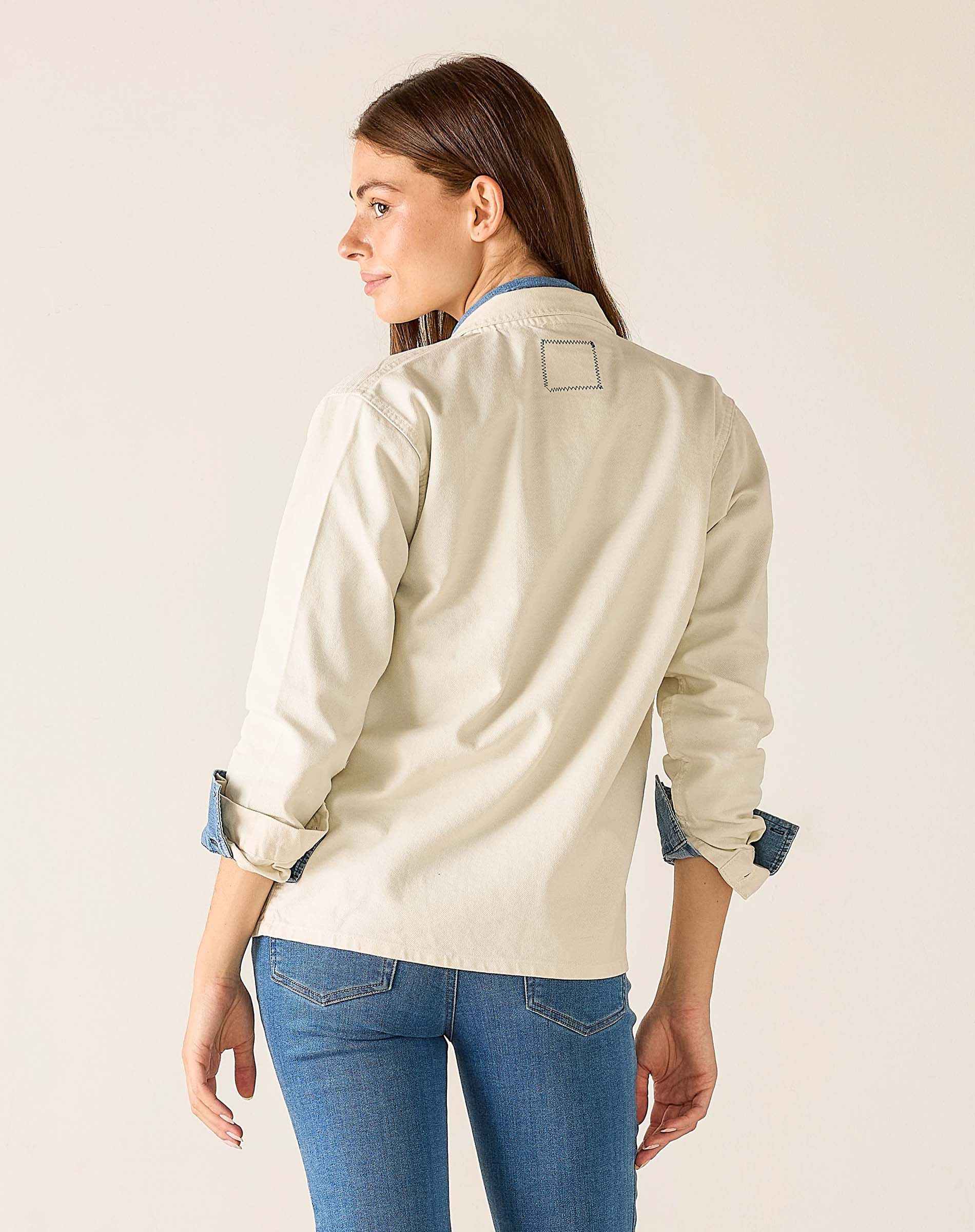 Woman wearing a beige jacket and blue jeans on a plain background
