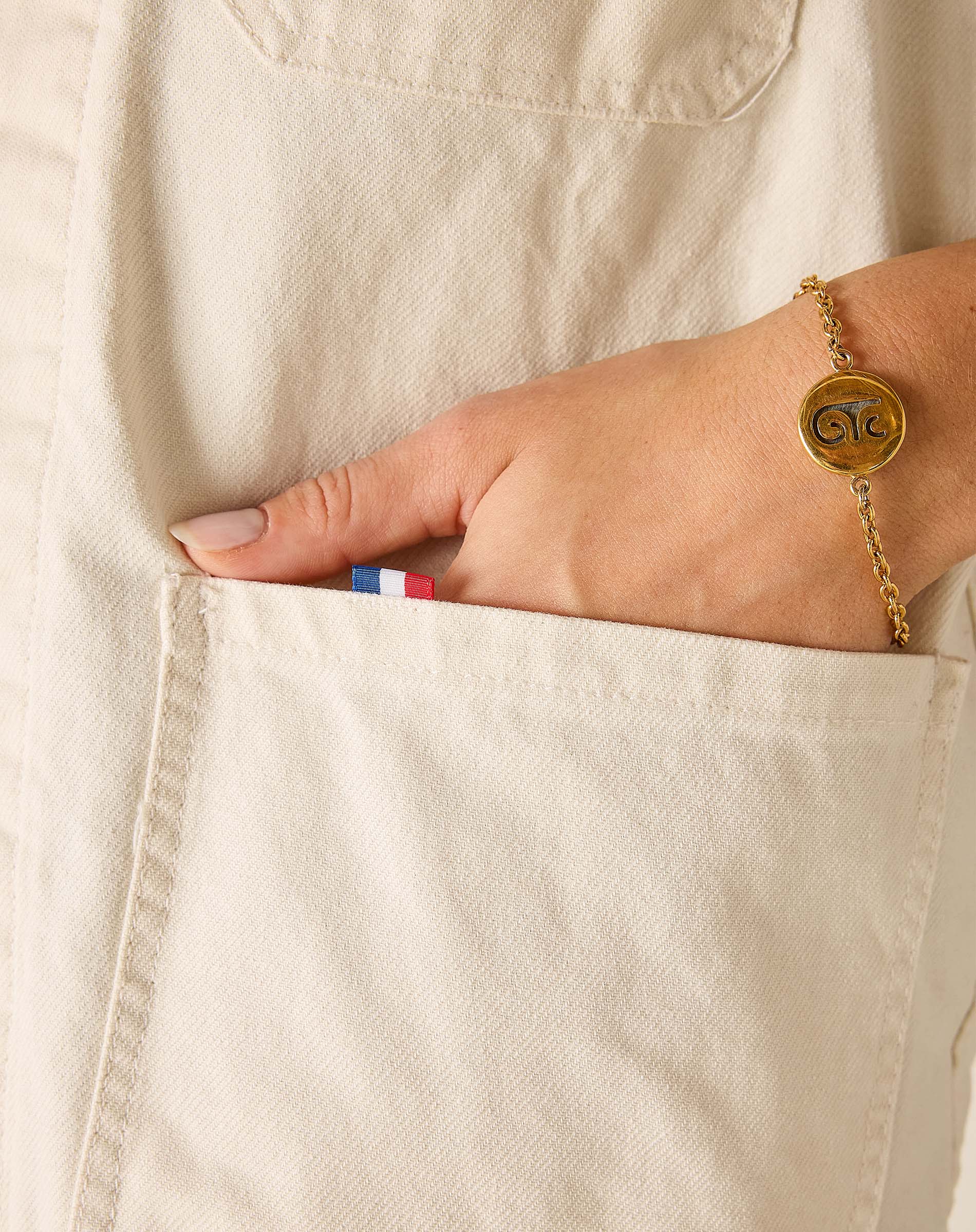 Hand with a gold bracelet on a beige fabric background