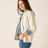 Woman wearing a cream blazer over a denim shirt and jeans on a plain background