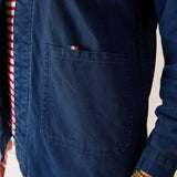 Navy blue shirt with a pocket and red and white striped sleeve on a neutral background