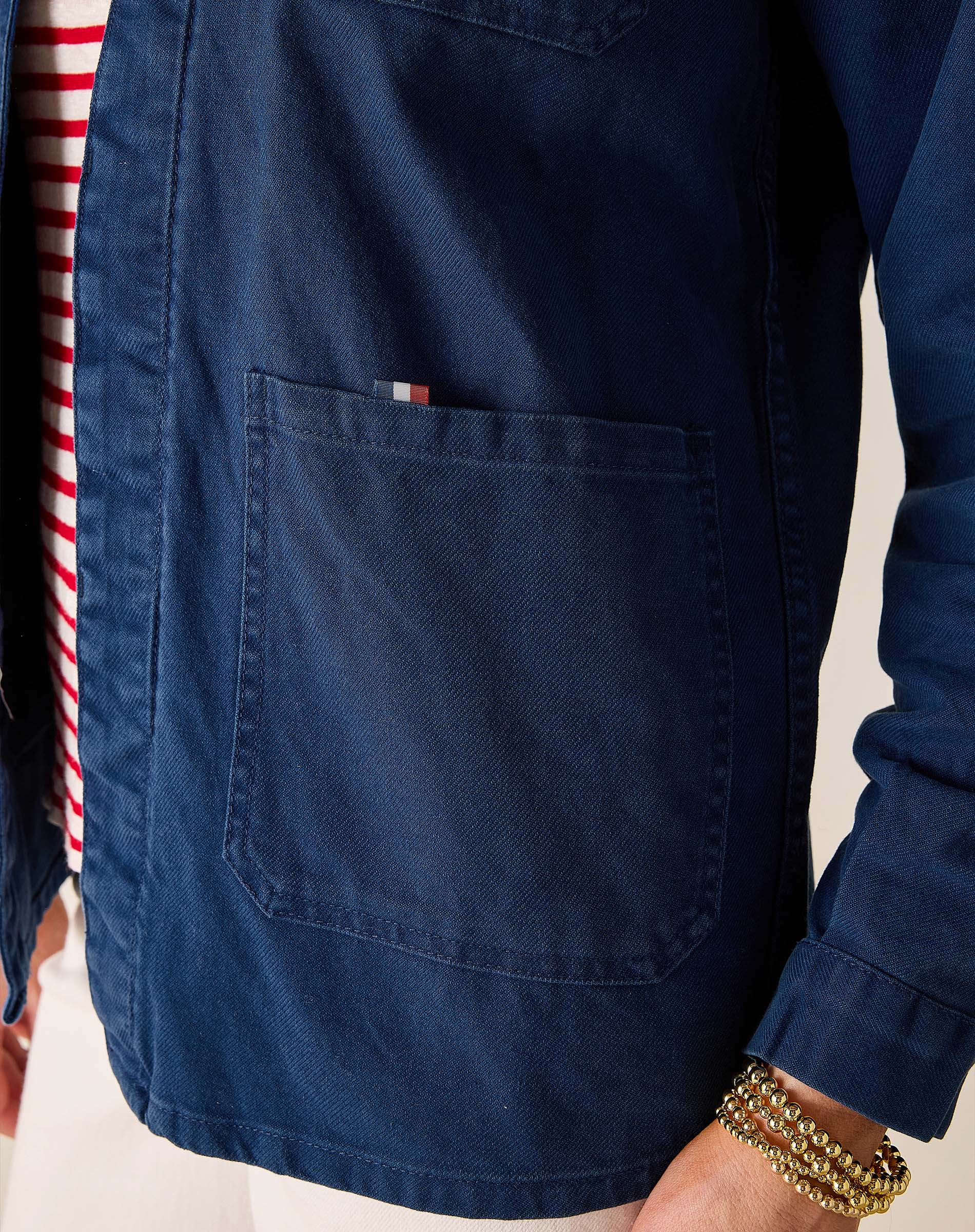 Navy blue shirt with a pocket and red and white striped sleeve on a neutral background