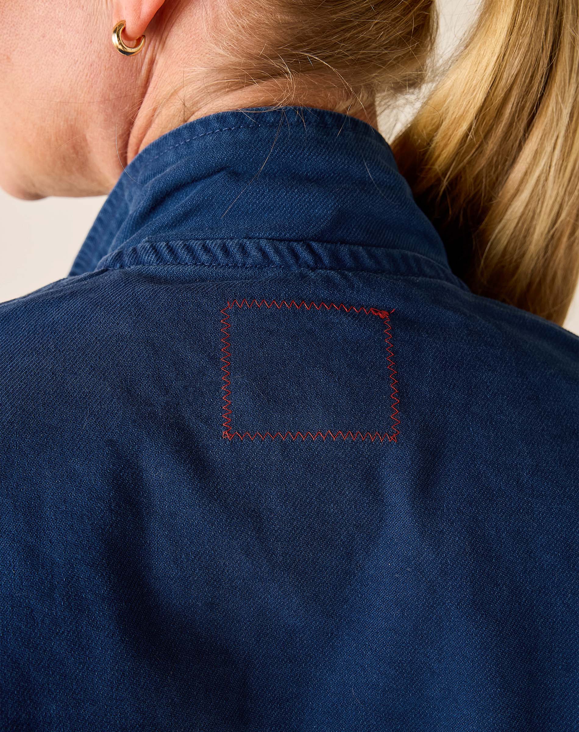 Close-up of a person wearing a blue jacket with a red-stitched pocket.