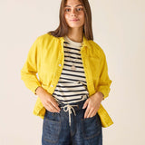 Woman wearing a yellow jacket, striped shirt, and blue jeans on a beige background