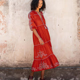Woman wearing a red dress with white embroidery against a textured wall.