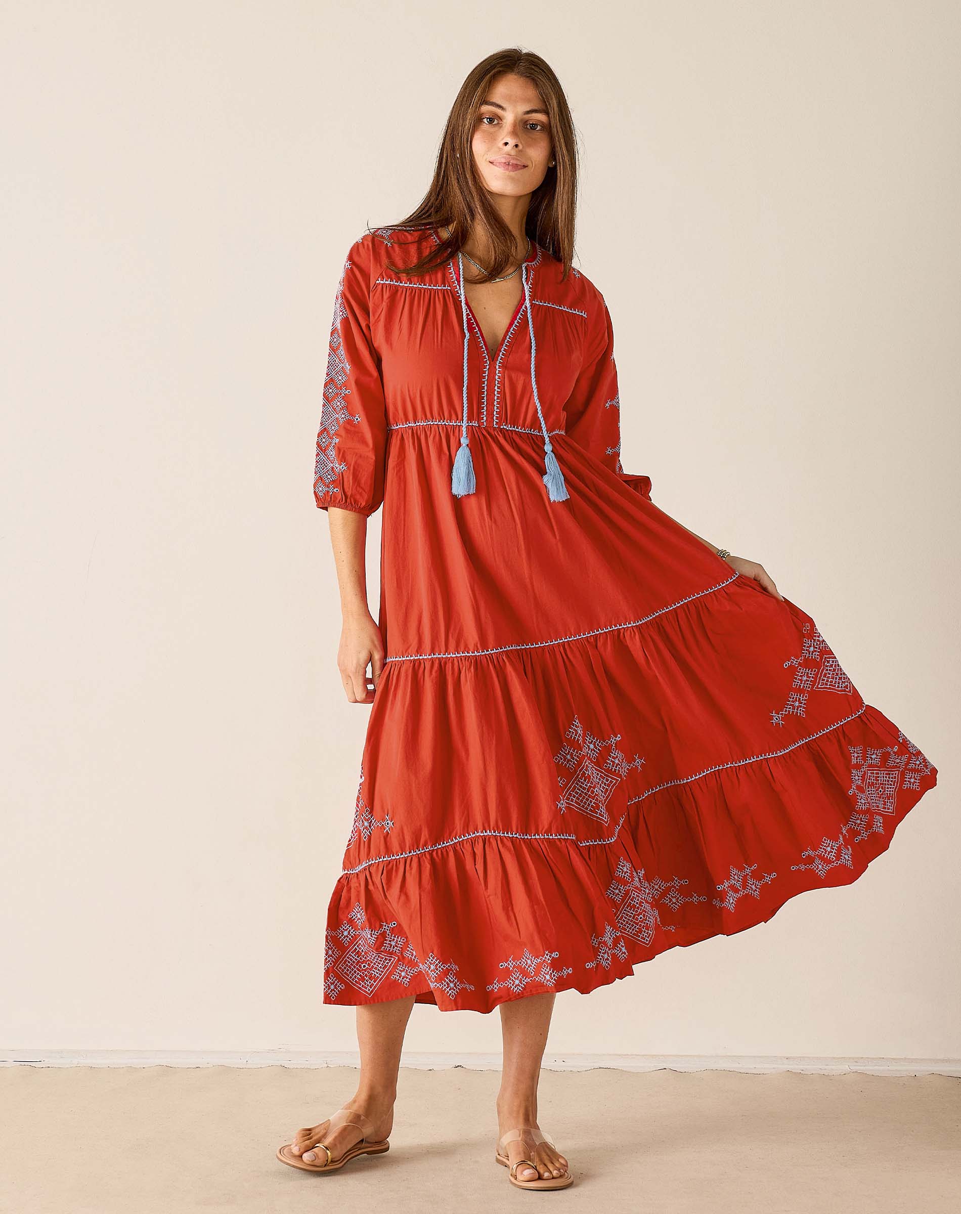 Woman wearing a red dress with floral embroidery on a beige background