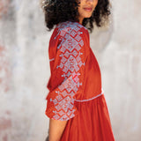 Woman wearing a red dress with white embroidery against a blurred background