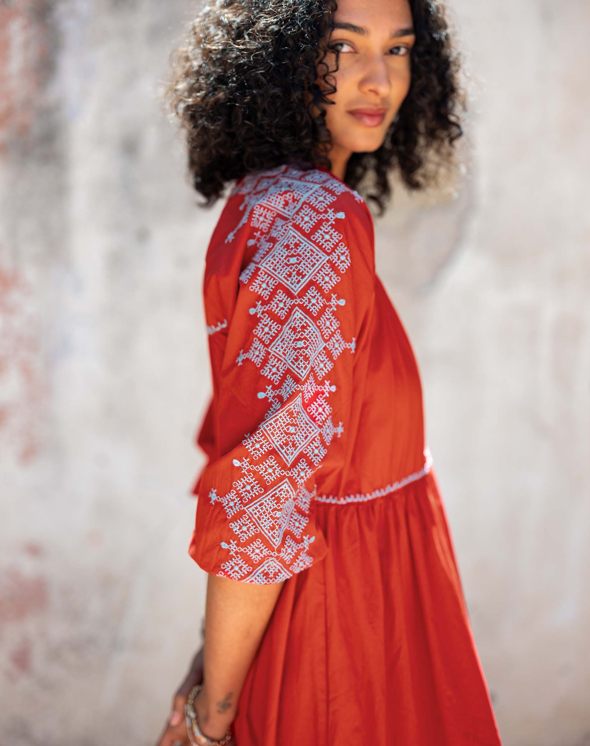 Woman wearing a red dress with white embroidery against a blurred background