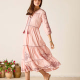 Woman wearing a pink dress with floral embroidery standing in front of a neutral background.