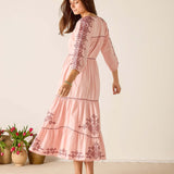 Woman wearing a pink dress with floral embroidery standing against a plain background