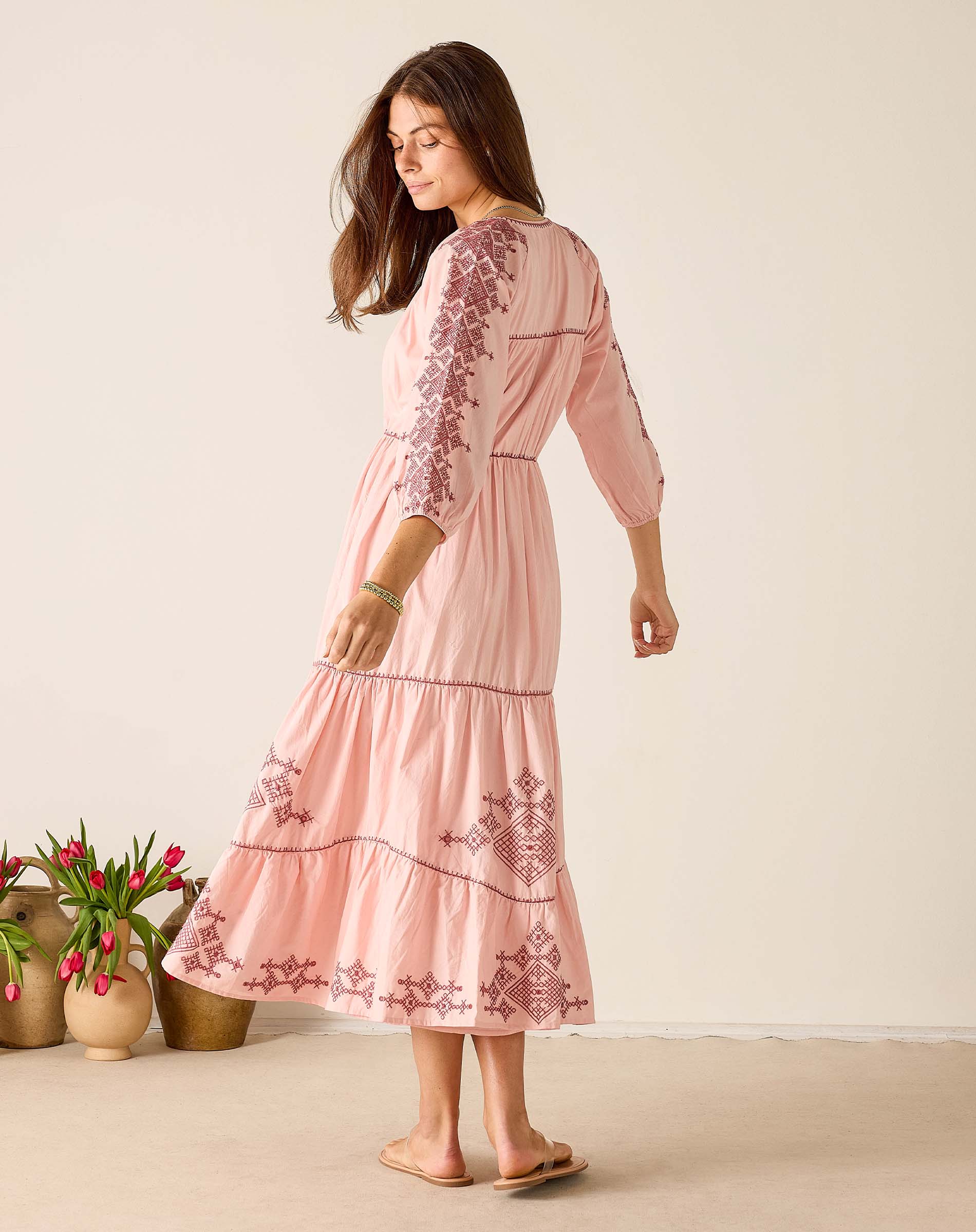 Woman wearing a pink dress with floral embroidery standing against a plain background