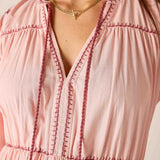 Close-up of a pink dress with intricate stitching details and a gold necklace.