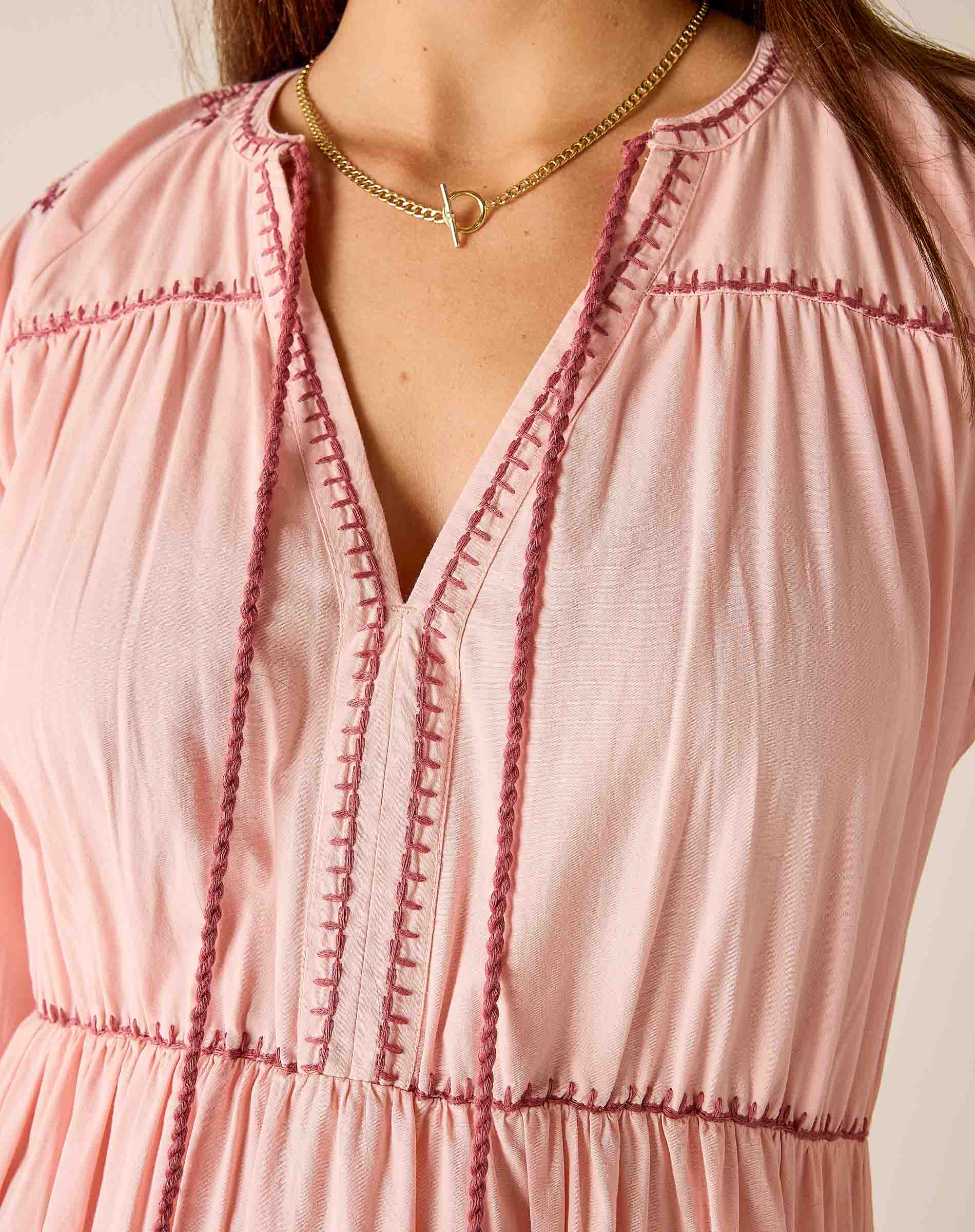 Close-up of a pink dress with intricate stitching details and a gold necklace.