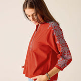 Woman wearing a red blouse with white embroidery on a beige background