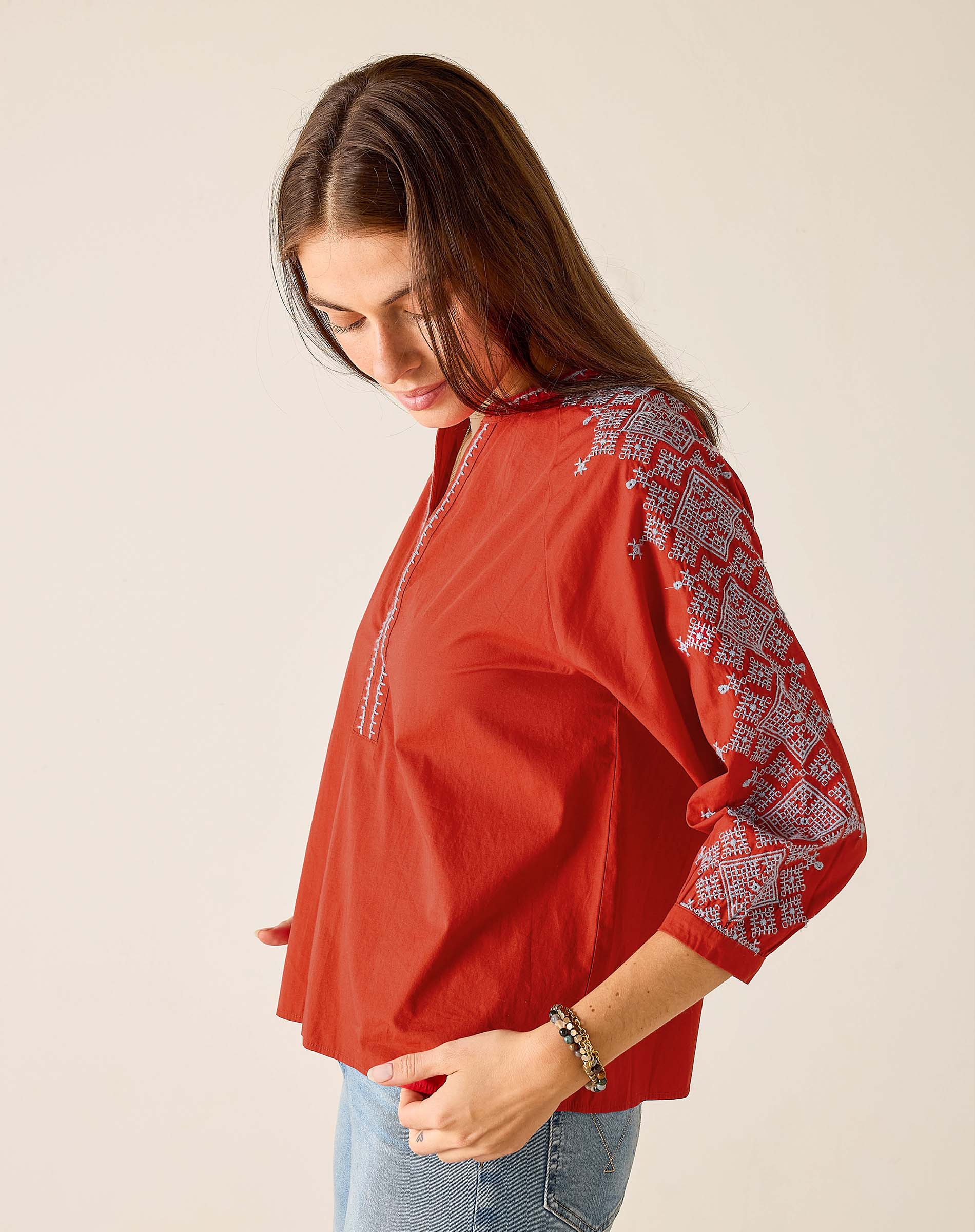 Woman wearing a red blouse with white embroidery on a beige background