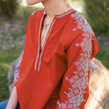 Red blouse with white embroidery worn by a person outdoors.