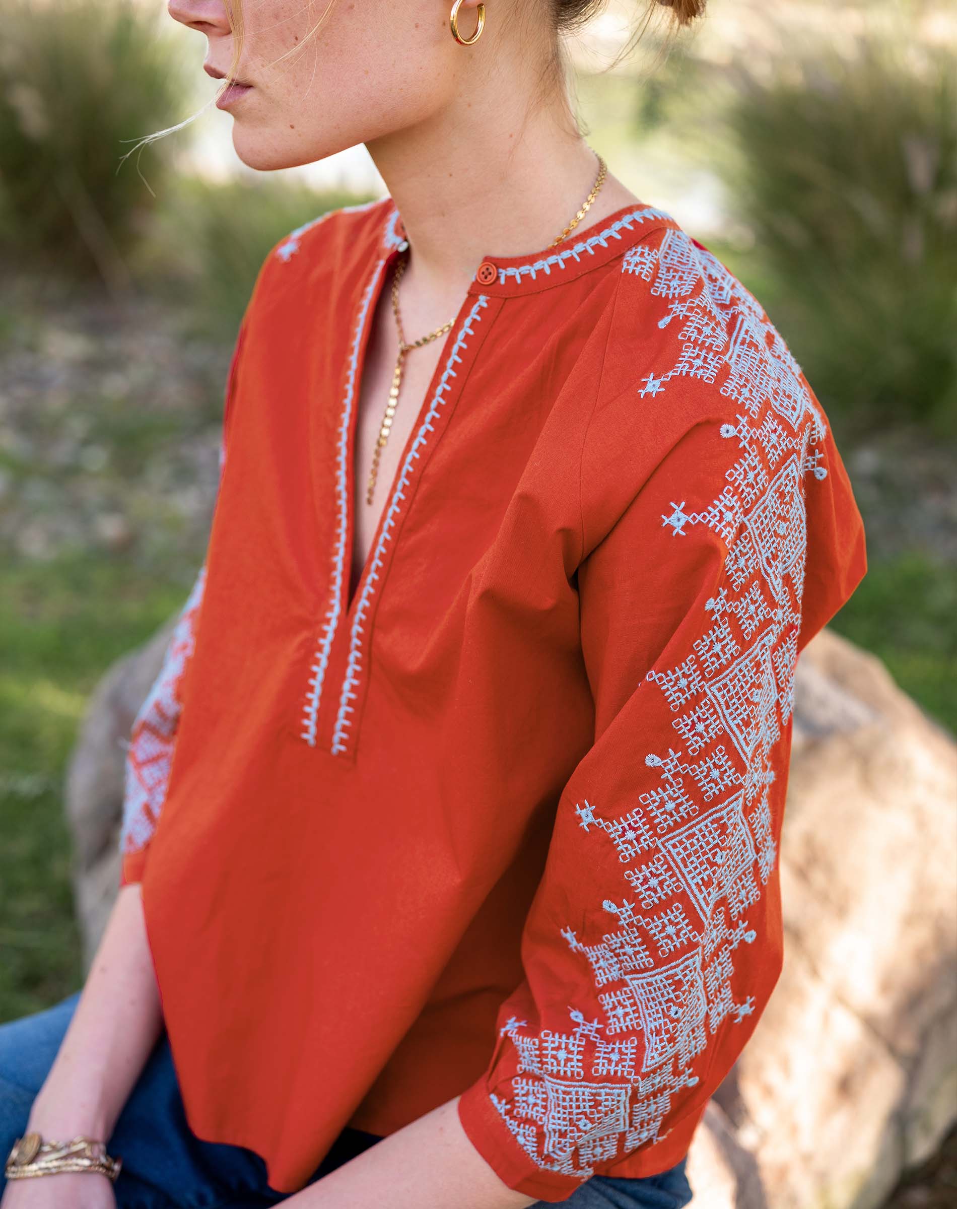 Red blouse with white embroidery worn by a person outdoors.