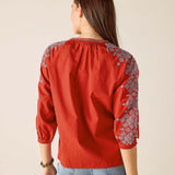 Red embroidered blouse worn by a person on a beige background